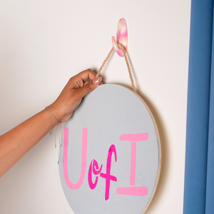 Hand holding a circular sign with 'UofI' in pink letters against a light background