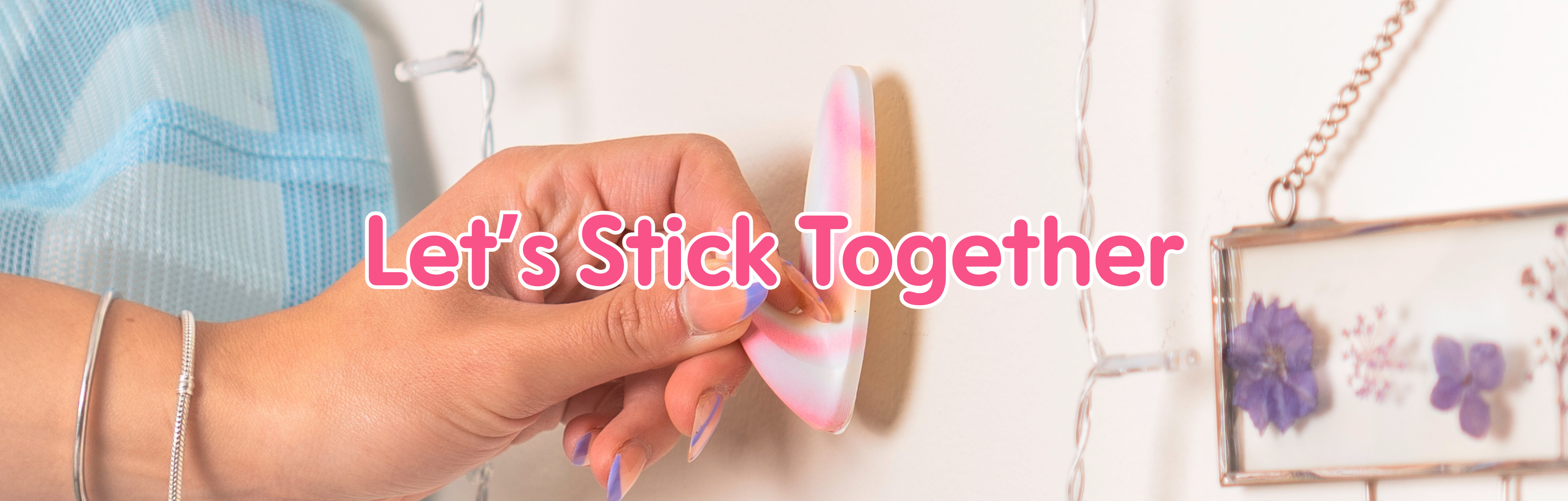 Hand placing a colorful WallCandy adhesive hook on a decorated wall with text overlay “Let’s Stick Together.