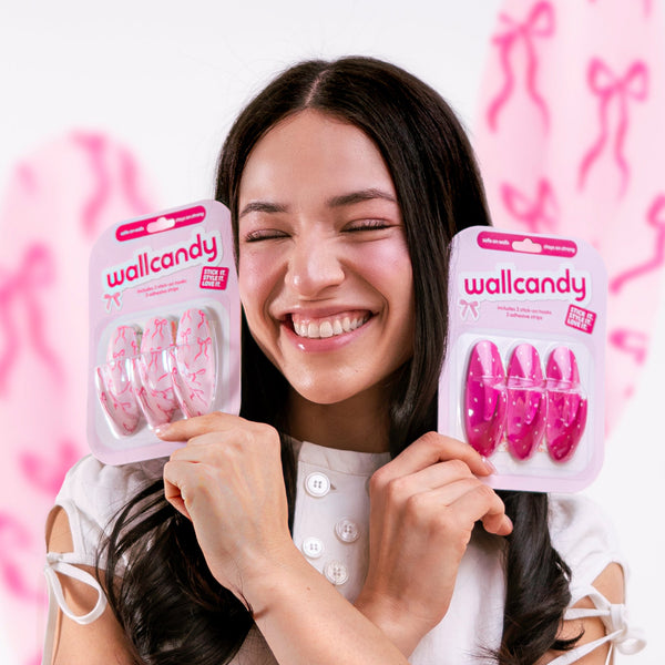 Woman holding two packages of wallcandy products against a pink background