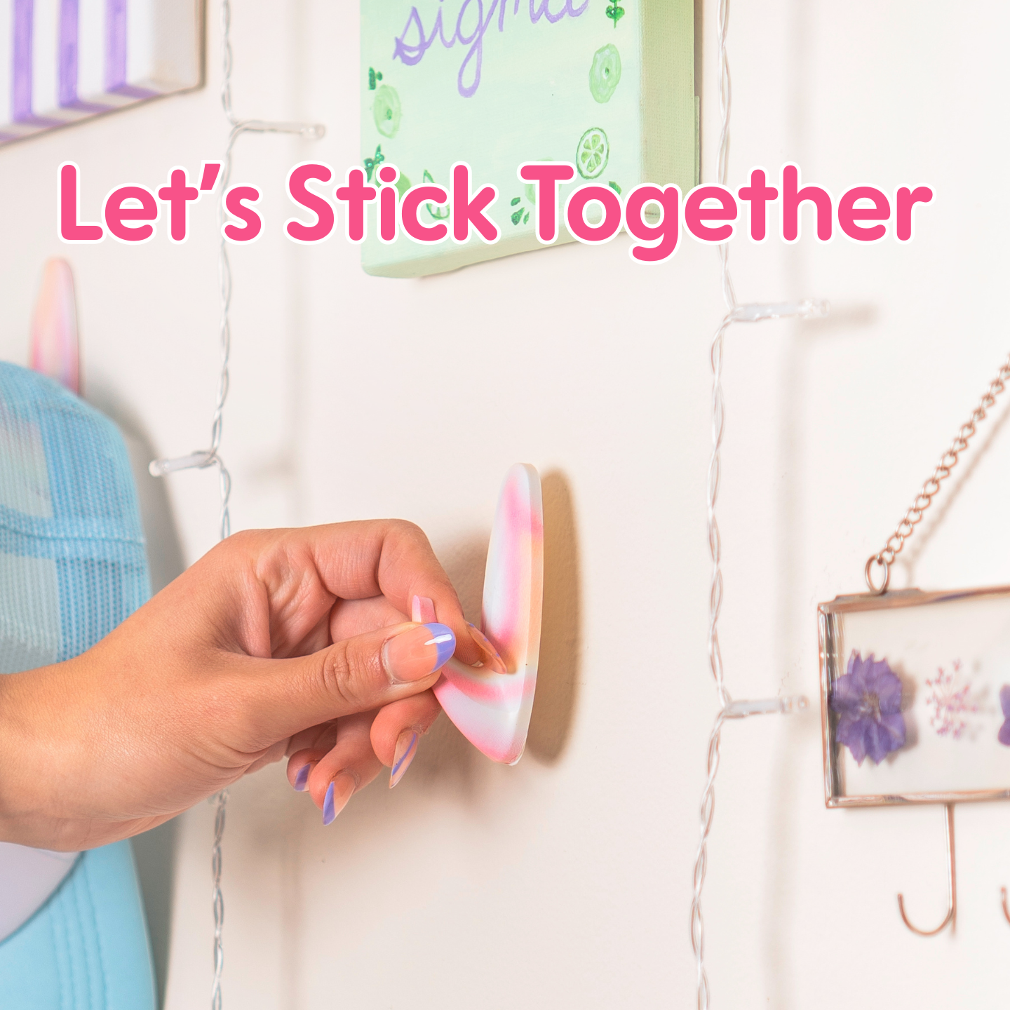Hand placing a colorful WallCandy adhesive hook on a decorated wall with text overlay “Let’s Stick Together.”