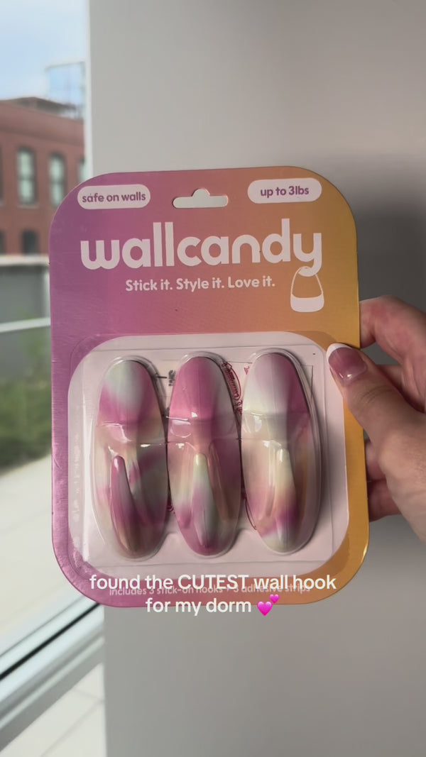 Hand holding a WallCandy Ombre Hook pack (pink, purple, and yellow gradient) with text overlay “found the CUTEST wall hook for my dorm 💕