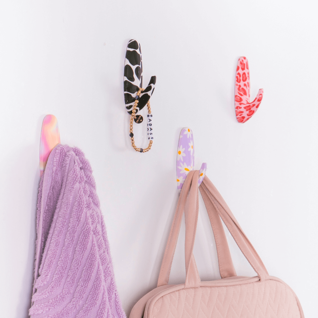 Decorative hooks with animal print designs on a white wall, holding a pink bag and purple towel.