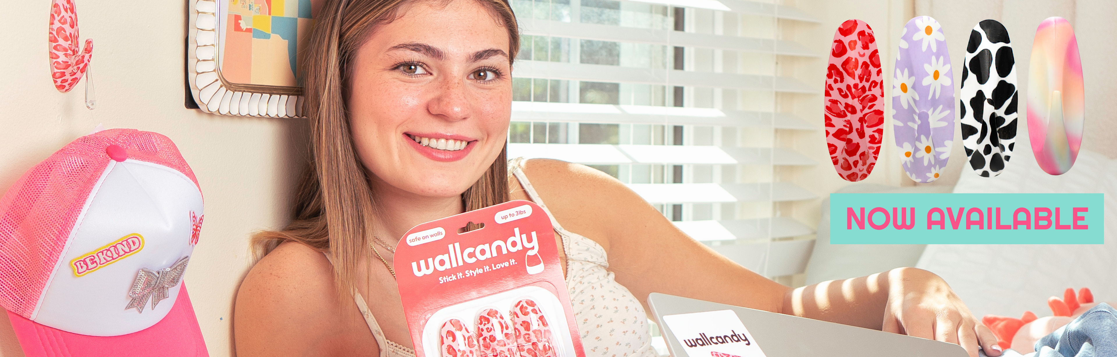 Woman holding WallCandy hook package with multiple colorful wall hook designs displayed and text showing now available.
